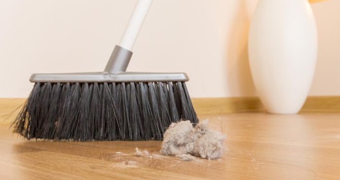 using broom on hardwood floor to clean dirt and debris